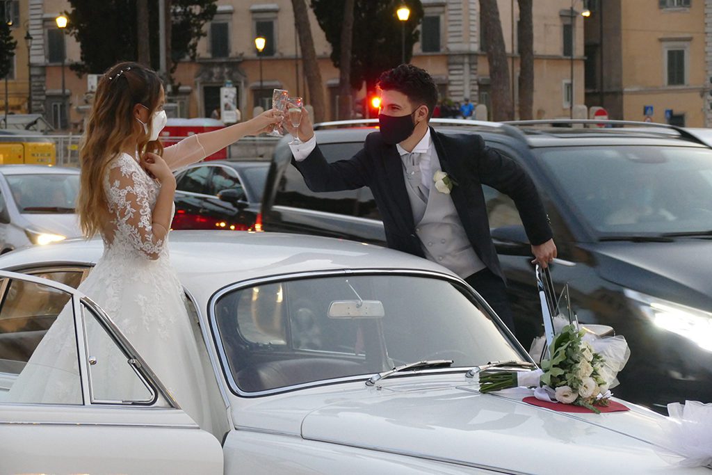 Married couple clinking glasses on the Piazza Venezia, wearing masks