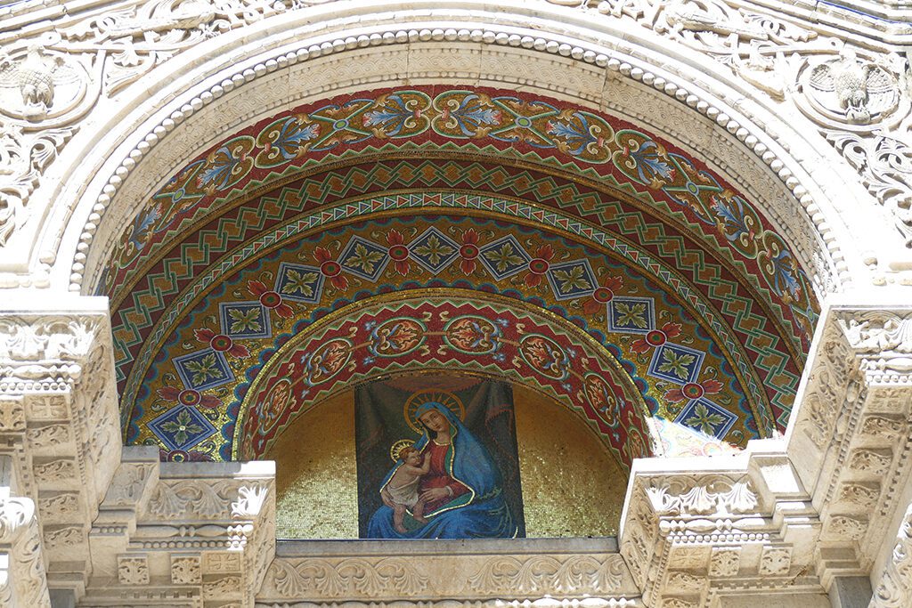 The central portal, artistically carved from wood. It shelters the richly decorated mosaic of Our Lady of the Snow in La Spezia.