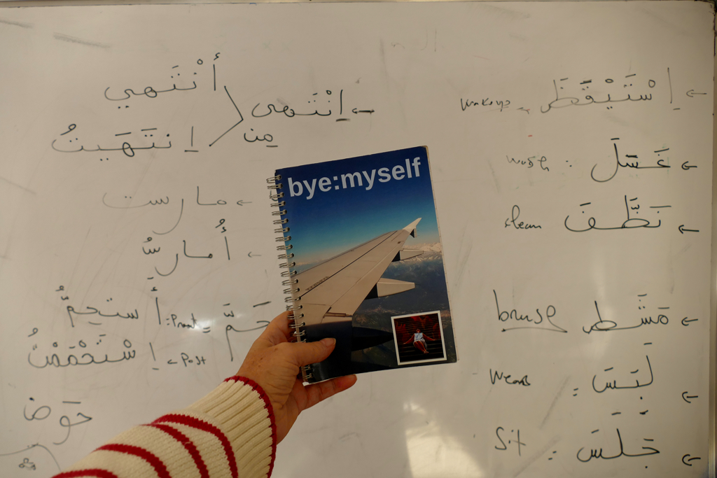byemyself's notebook in front of a whiteboard with Arabic writing