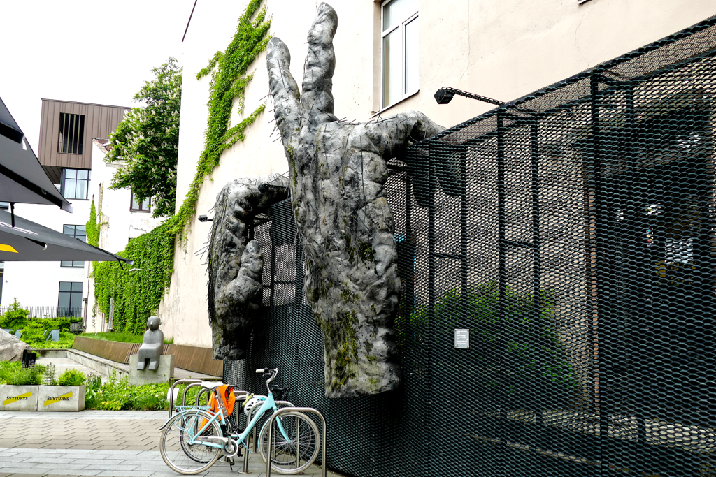 The hands of Donatas Jankauskas-Duonis, titled Viktoras ar Viktorija, clasp the fence. In the background, Ksenija Jaroševaite's granite sculpture, appropriately titled Sedinti, hence, Sitting.