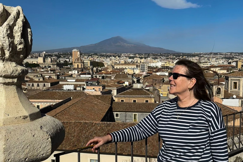Renata Green standing on the balcony of the Chiesa della Badia di Sant'Agata church with the Etna in the backdrop.