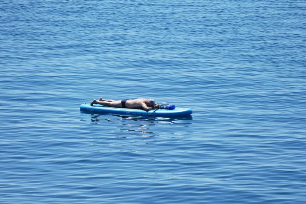 Man laying on a board off the coast of Nervi. 