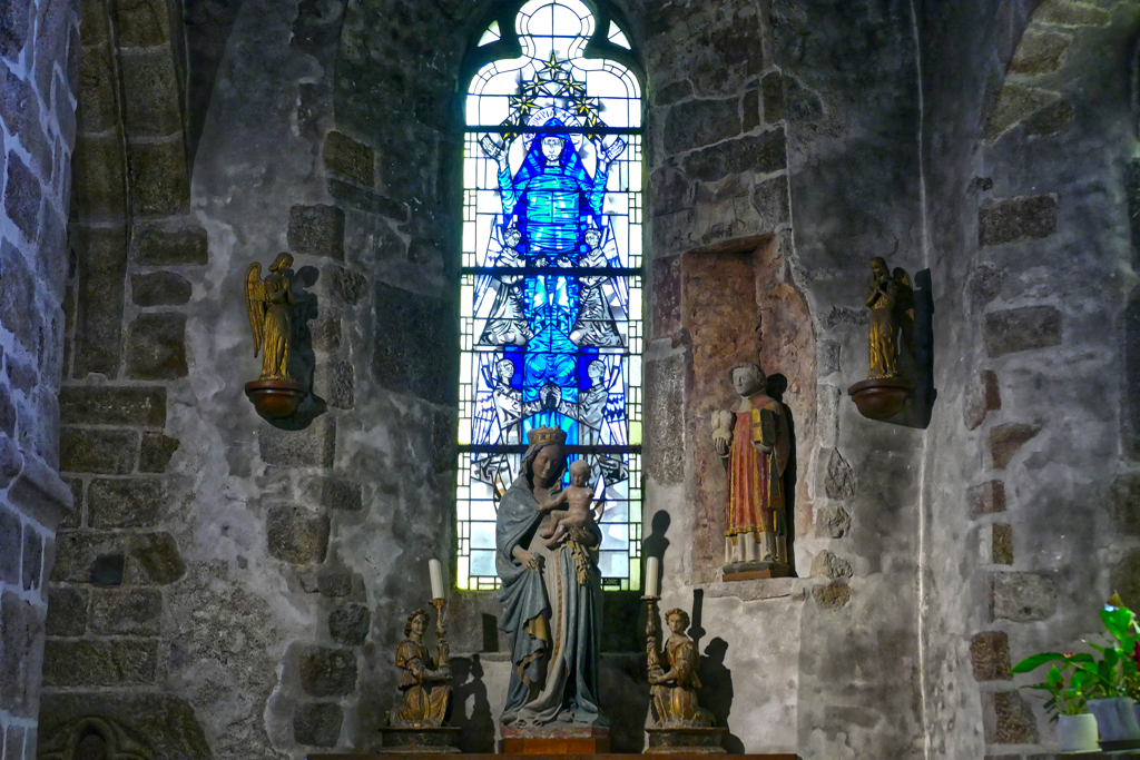 Sanctuary with a blue stained glass window and a statue of Mary at the Église Saint-Pierre.